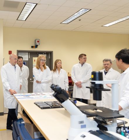 穿着白色实验服的人站在实验室的显微镜前。
